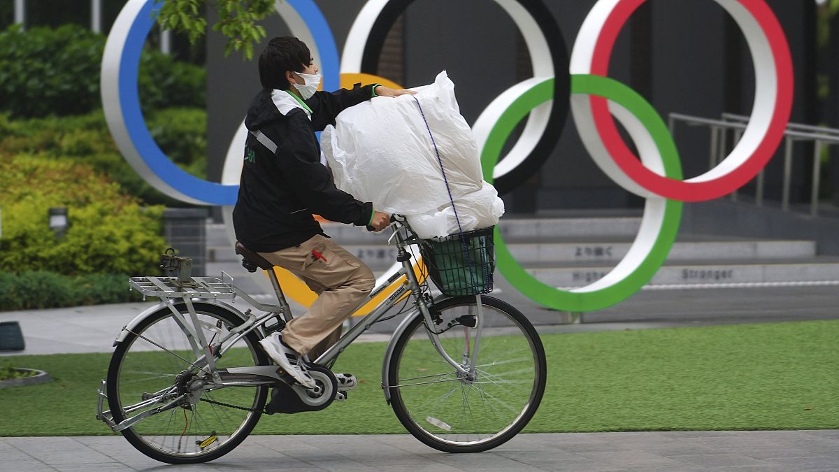 Az olimpiai ötkarika előtt halad el egy védőmaszkos kerékpáros Tokióban 2021. május 13-án.