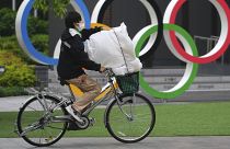 Az olimpiai ötkarika előtt halad el egy védőmaszkos kerékpáros Tokióban 2021. május 13-án.