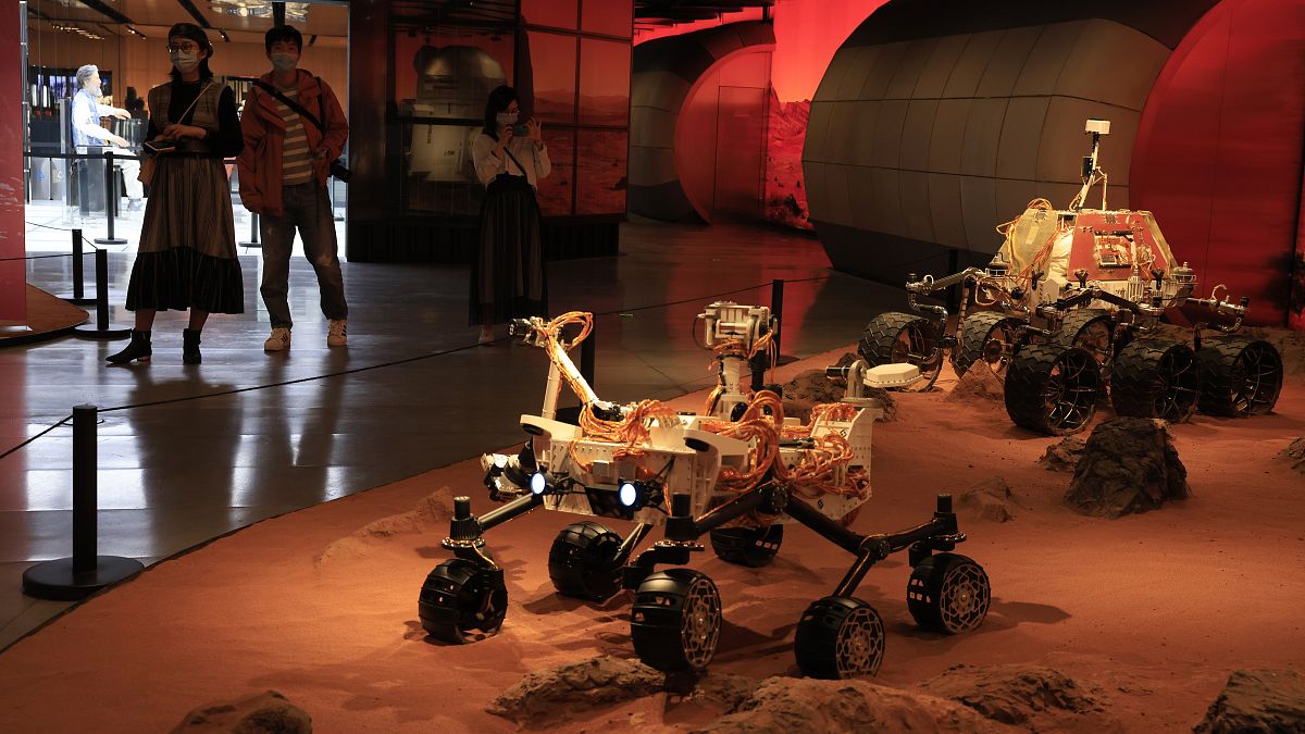 Visitors pass by an exhibition depicting rovers on Mars in Beijing on Friday, May 14, 2021. 