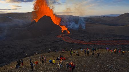 People watch as lava flows from an eruption from the Fagradalsfjall volcano on the Reykjanes Peninsula in southwestern Iceland on Tuesday, May 11, 2021.