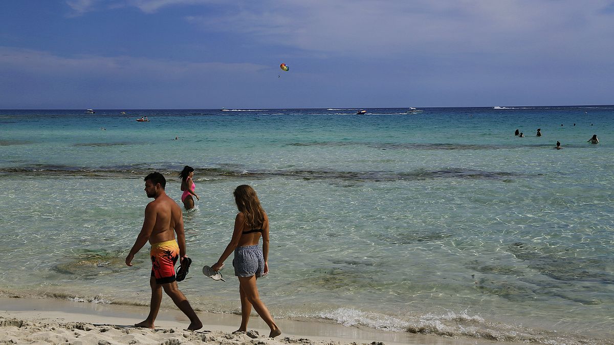 A couple walk at the beach as other enjoy the sea water in the southeast resort of Ayia Napa in Cyprus