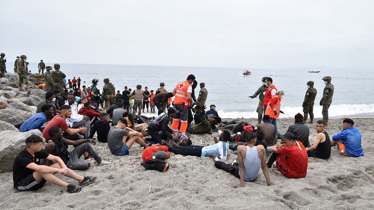 يساعد أعضاء الصليب الأحمر المهاجرين الذين وصلوا سباحة إلى جيب سبتة الإسباني بحضور الجنود الإسبان وأفراد الحرس المدني الإسبان في 18 مايو / أيار 2021 في سبتة.