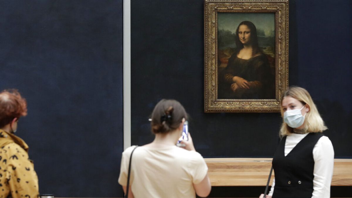 Visitante posa com máscara em frente à Mona Lisa, no Museu do Louvre