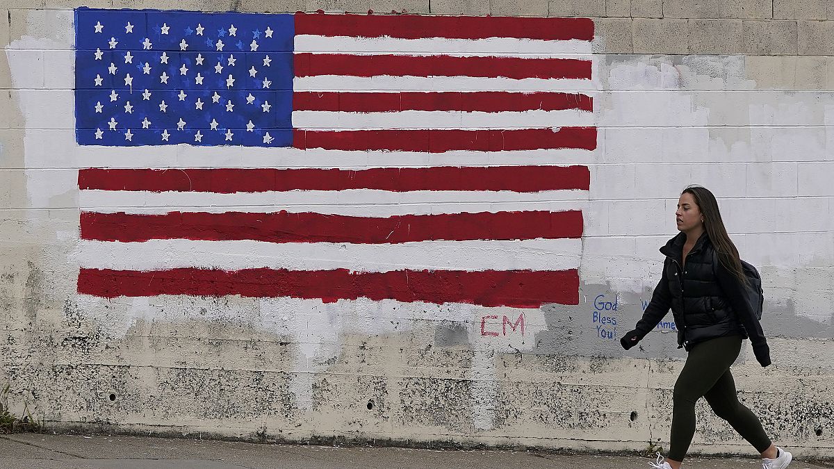 فتاة أمريكية تسير بجانب حائط رُسم عليه علم الولايات المتحدة في أحد شوارع سان فرانسيسكو