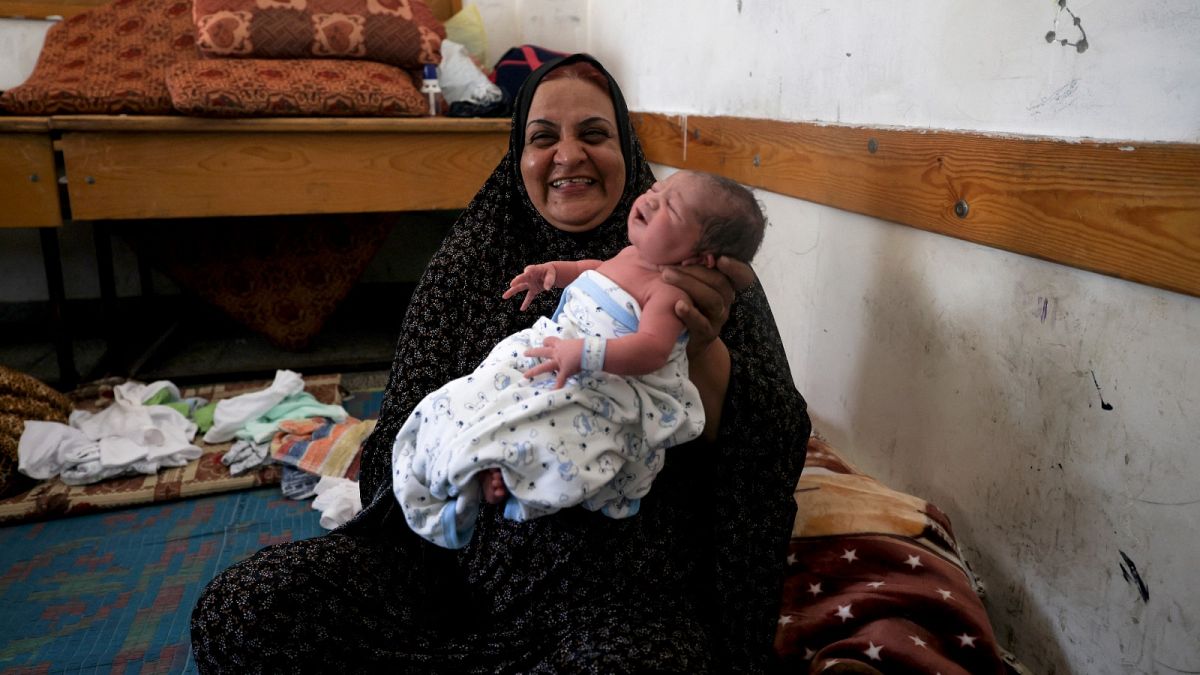 امرأة فلسطينية تحمل رضيعا يبلغ من العمر يوما واحدا في إحدى مدارس الأمم المتحدة حيث تلجأ عائلات فلسطينية فقد منازلها بالقصف- غزة