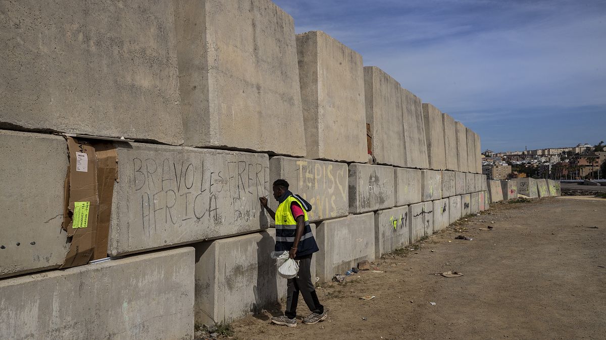 Un migrante subsahariano escribe su nombre en el espigón de la ciudad española de Ceuta, en el norte de África