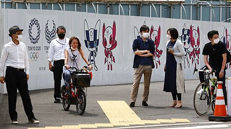 People stand by posters to promote the Tokyo Olympic Games scheduled to start in the summer of 2021, in Tokyo, Monday, May 24, 2021.
