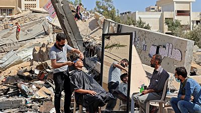 هاشم الجروشة، حلاق فلسطيني يعمل وسط أنقاض مبان ومتاجر دمرتها الغارات الإسرائيلية  في مدينة غزة. 25 مايو 2021.