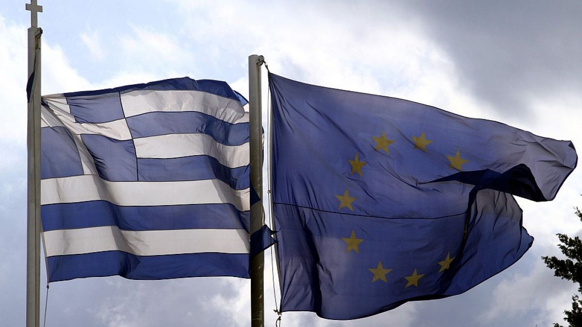 Οι σημαίες της Ελλάδας και της Ευρωπαϊκής Ένωσης ανεμίζουν με φόντο τον αττικό ουρανό.