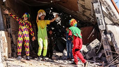 فلسطينيون يرتدون زي المهرجين يستمتعون بالأطفال وسط أنقاض مبنى دمر خلال القصف الإسرائيلي الأخير في رفح ، جنوب قطاع غزة