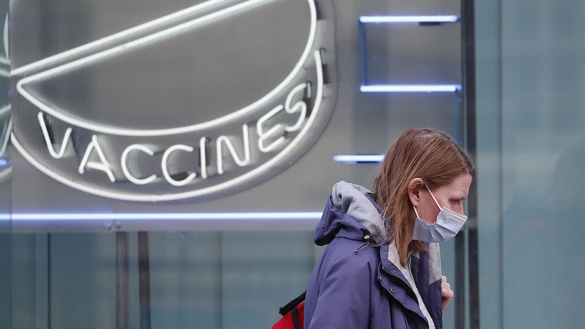 Una mujer con una máscara contra el coronavirus pasa por delante de un cartel de neón en el Instituto Wellcome de Londres, el martes 2 de febrero de 2021. 