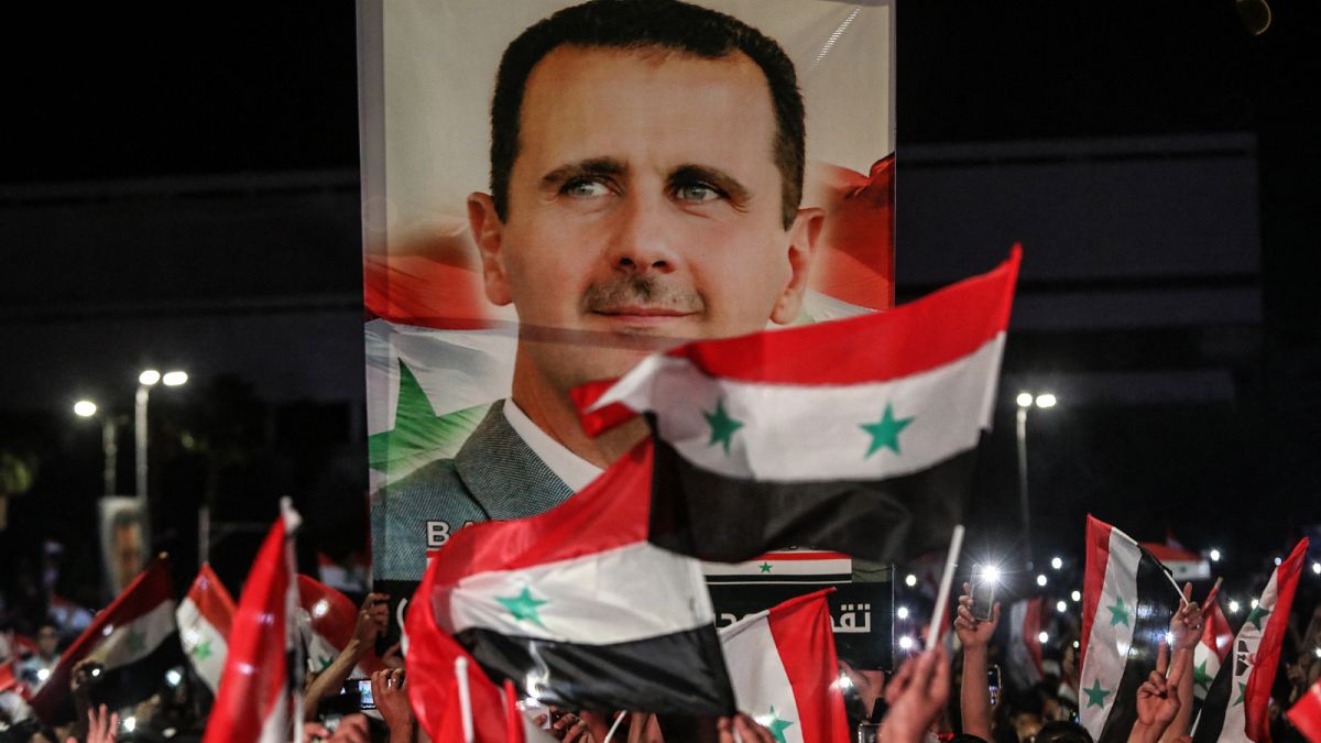 سوريون يلوحون بالأعلام الوطنية ويحملون صورة كبيرة لرئيسهم وهم يحتفلون في شوارع العاصمة دمشق.
