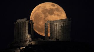 The flower supermoon rises behind the columns of the ancient marble temple of Poseidon at Cape Sounion, about 70 Km south of Athens. May 26, 2021