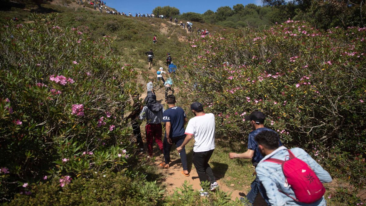 أشخاص يعبرون غابة قرب مدينة الفنيدق الحدودية شمال المغرب في طريقهم إلى جيب سبتة الإسباني يوم الثلاثاء 18 أيار/مايو 2021