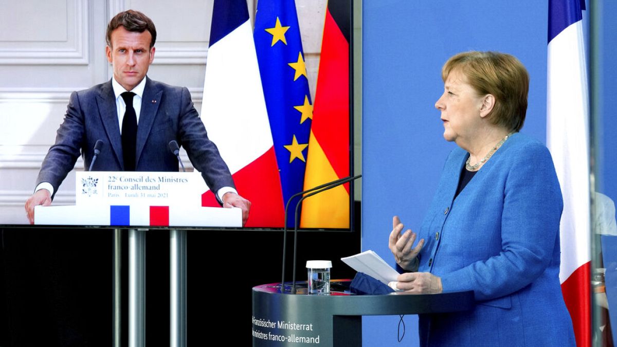 French President Emmanuel Macron is seen on a video screen during a joint press conference with German Chancellor Angela Merkel