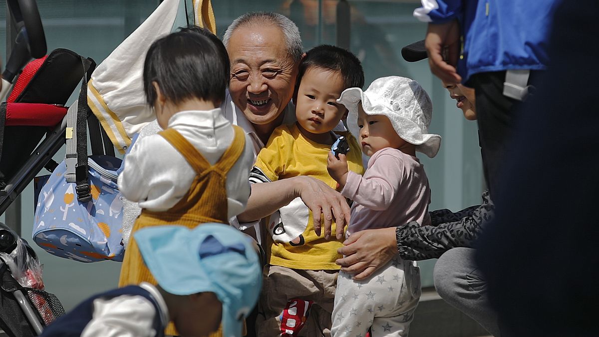 An elderly man plays with children near a commercial office building in Beijing on May 10, 2021. 