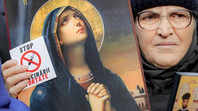 An anti-vaccination protester holds a sticker that reads "Stop the Mandatory Vaccination" next to an icon during a rally in Bucharest, Romania, Saturday, March 20, 2021. An anti-vaccination protester holds a sticker that reads "Stop the Mandatory Vaccination" next to an icon during a rally in Bucharest, Romania, Saturday, March 20, 2021.