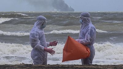 Sri Lankan navy soldiers clad in protective suits discuss as they clean debris washed ashore