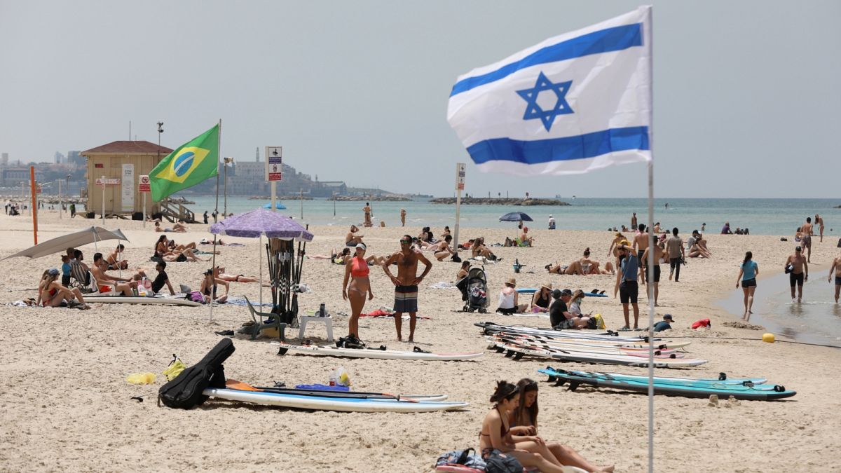 Tavaly májusi fotó: emberek napoznak és sétálnak egy tengerparti strandon Tel-Avivban
