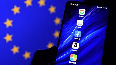 Logos of Google, Apple, Facebook, Amazon and Microsoft displayed on a mobile phone with an EU flag displayed in the background
