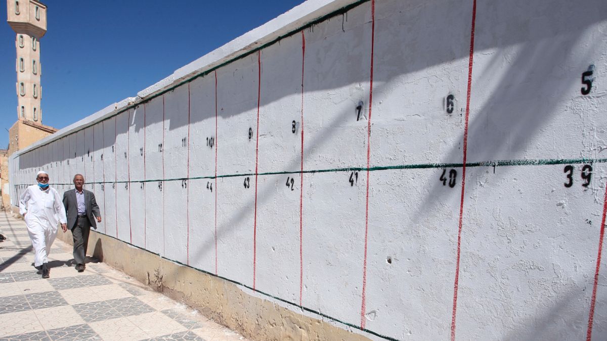 جزائريان يمران بجانب حائط محصص لملصقات المرشحين الانتخابيين