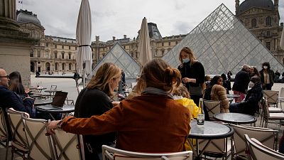 People drink outdoors on a bar terrace in front of the Louvre museum in Paris, Thursday, May 20, 2021. 