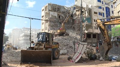 Bulldozer bringing down a building, that had part of it destroyed in an Israeli strike