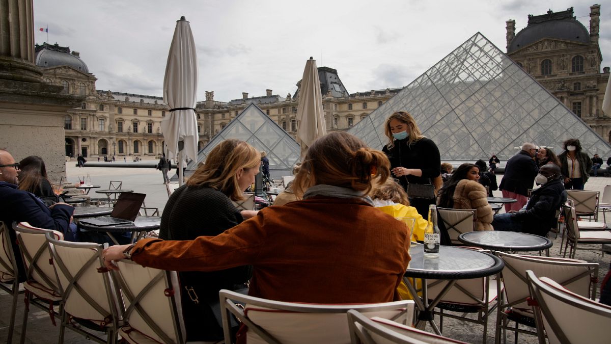 أشخاص يجلسون في شرفة إحدى المقاهي المطلة على متحف اللوفر وسط العاصمة الفرنسية باريس.