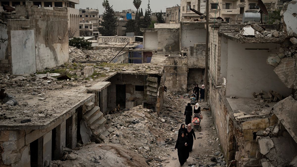 Suriye'nin İdlib kentinde, yoğun bombardıman sonucu harabeye dönen bir mahalleden geçen kadınlar (arşiv) 