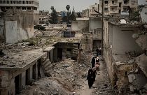 Suriye'nin İdlib kentinde, yoğun bombardıman sonucu harabeye dönen bir mahalleden geçen kadınlar (arşiv) 