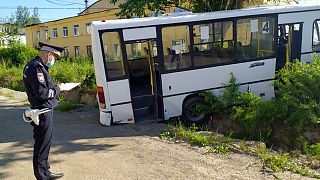 A Russian police officer stands near the damaged bus.