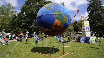 People gather around a giant globe during a climate demonstration at Kimberley Park in Falmouth, Cornwall, England, Saturday, June 12, 2021.