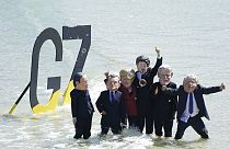 Des manifestants, les pieds dans l'eau, portent des masques représentant les dirigeants du G7, à Saint Ives, Royaume-Uni, le 13 juin 2021