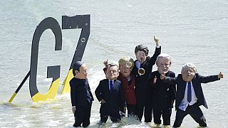 Des manifestants, les pieds dans l'eau, portent des masques représentant les dirigeants du G7, à Saint Ives, Royaume-Uni, le 13 juin 2021