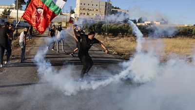 A Palestinian demonstrator returns a tear gas canister fired by Israeli forces.
