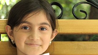 Una niña armenia refugiada sonríe durante la entrevista a su madre