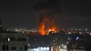 Explosions light-up the night sky above buildings in Gaza City as Israeli forces shell the Palestinian enclave, early on June 16, 2021.