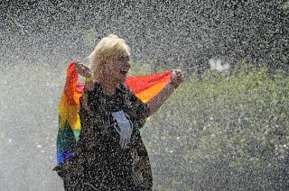 A woman with a rainbow flag cools off in a sprinkler ahead of the Equality Parade, the largest LGBT pride parade. Warsaw, Poland. June 19, 2021