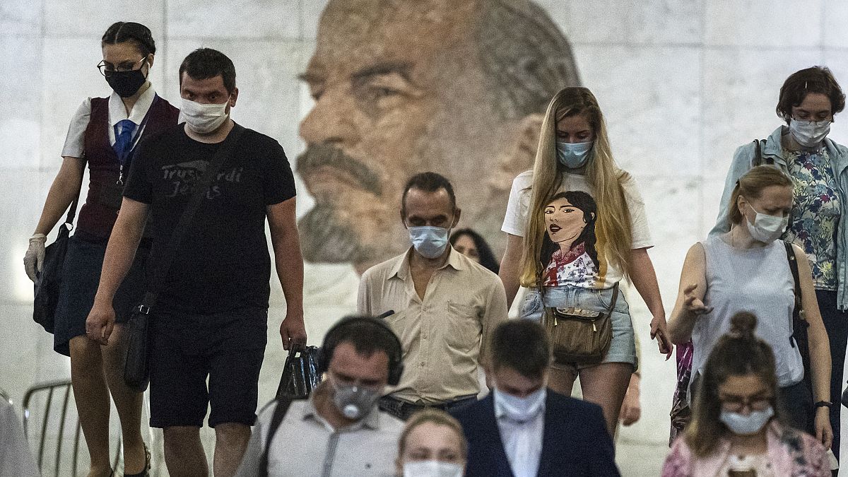 FILE: People wearing face masks walk through the subway, with a portrait of Soviet founder Vladimir Lenin in the background, in Moscow, Russia, June 10, 2021.  