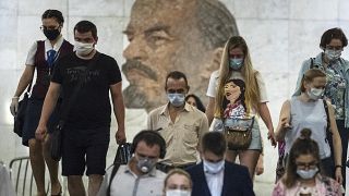 FILE: People wearing face masks walk through the subway, with a portrait of Soviet founder Vladimir Lenin in the background, in Moscow, Russia, June 10, 2021.  