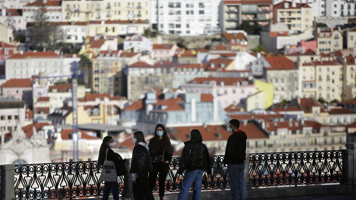 FILE - In this March 11, 2021 file photo, a group of young people wearing face masks chat at a viewpoint overlooking Lisbon's old center. 