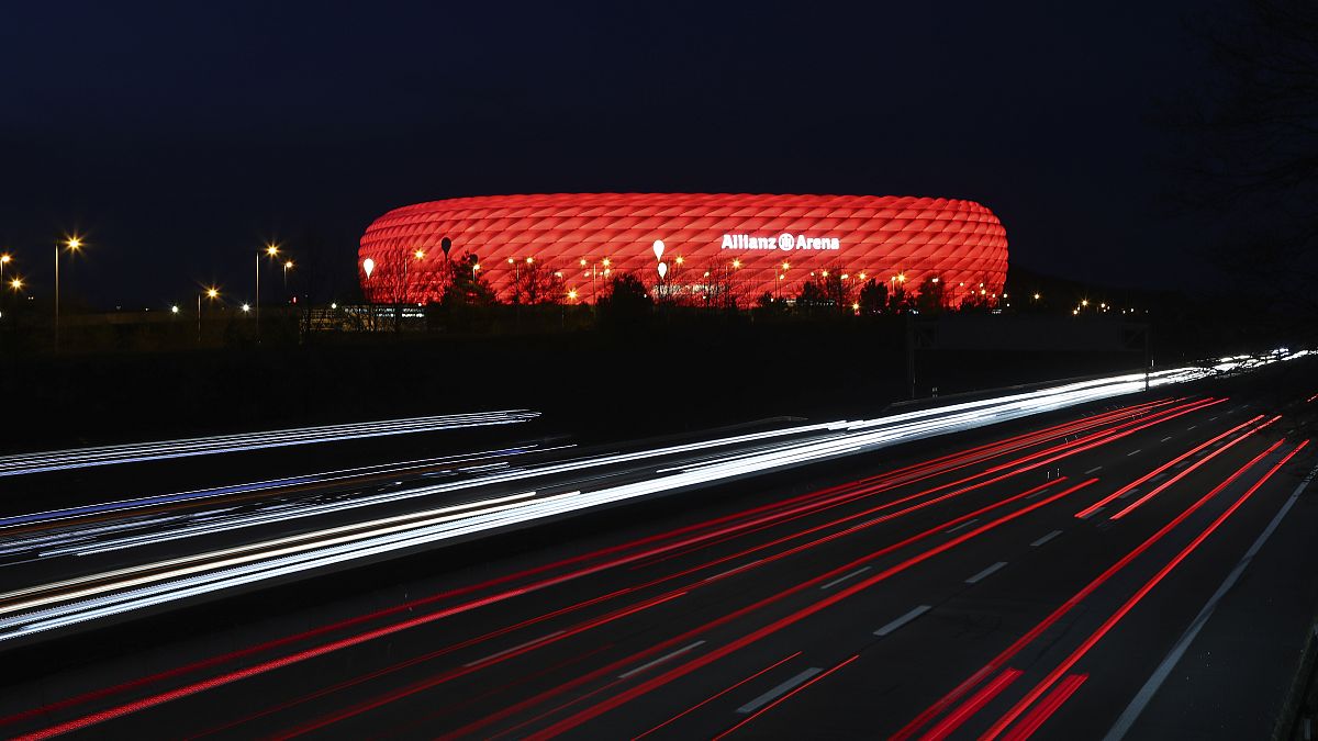 FILE - In this Monday, March 16, 2020 file photo, cars pass the illuminated 'Allianz Arena' soccer stadium in Munich, Germany. 