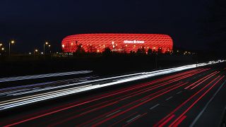 FILE - In this Monday, March 16, 2020 file photo, cars pass the illuminated 'Allianz Arena' soccer stadium in Munich, Germany. 