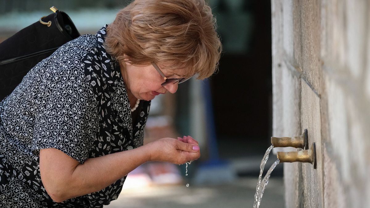 Nő iszik egy szarajevói közkútból 2021. június 21-én