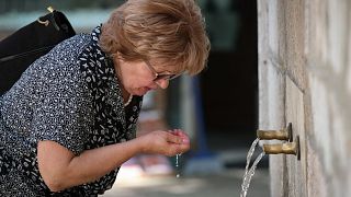 Nő iszik egy szarajevói közkútból 2021. június 21-én