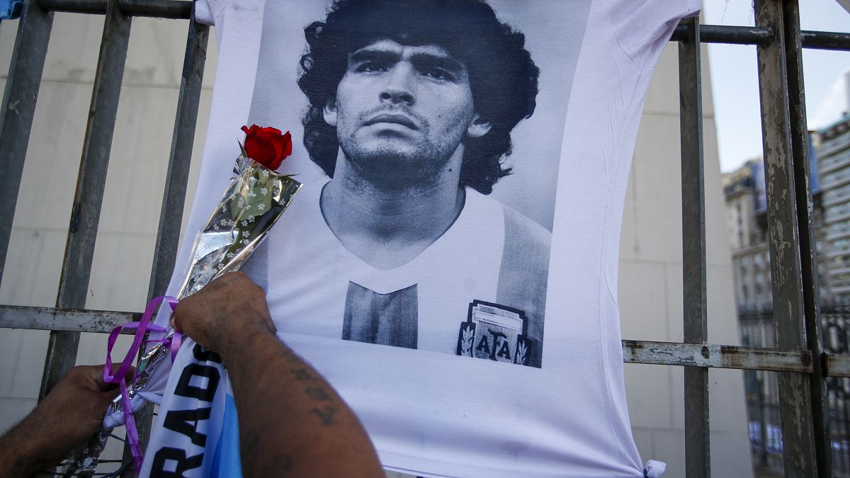رجل يضع وردة على صورة لنجم كرة القدم الراحل دييغو مارادونا خلال مسيرة للمطالبة بإجابات بخصوص وفاته، في بوينس آيرس، الأرجنتين.