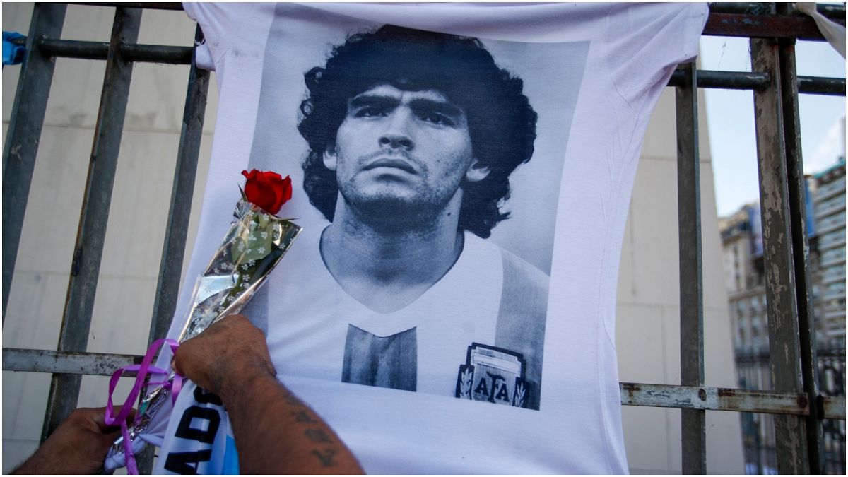 رجل يضع زهرة على قميص به صورة لنجم كرة القدم الراحل دييغو مارادونا-الأرجنتين