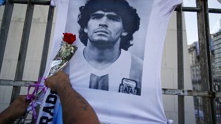 رجل يضع وردة على صورة لنجم كرة القدم الراحل دييغو مارادونا خلال مسيرة للمطالبة بإجابات بخصوص وفاته، في بوينس آيرس، الأرجنتين.