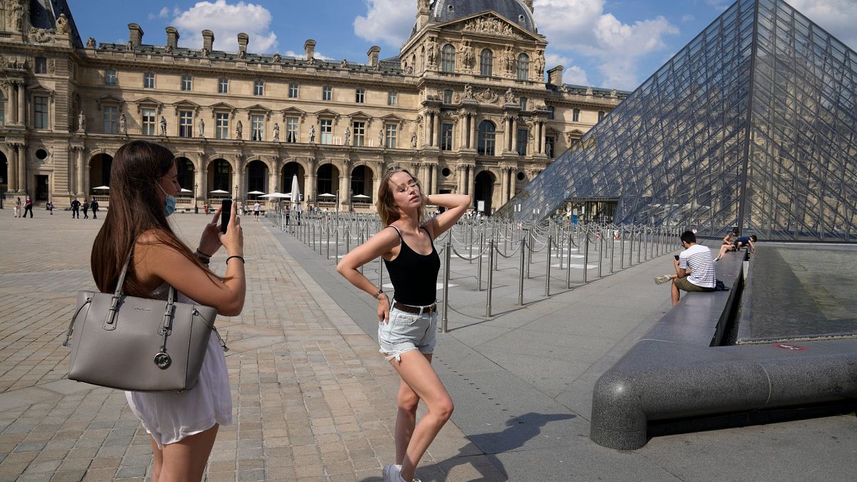 Two girls take pictures outside the Louvre Museum courtyard, in Paris, June 9, 2021 as France reopened its borders to foreign travellers.