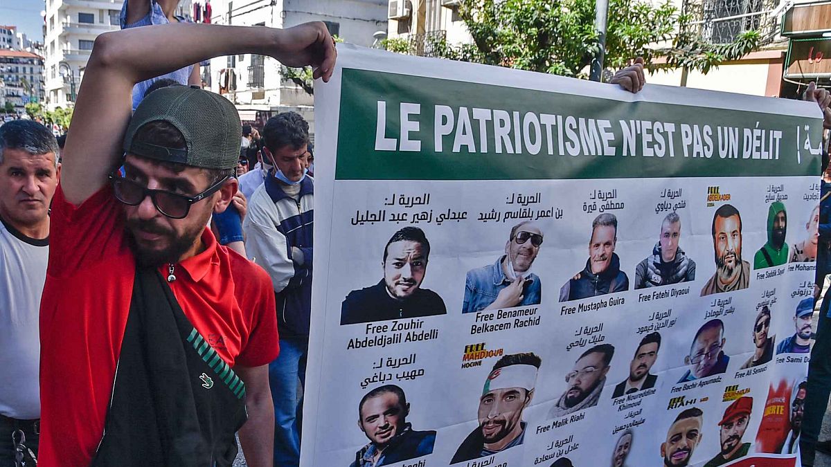 جزائريون يحملون لافتات عليها صور لنشطاء محتجزين في السجن، خلال مظاهرة مناهضة للحكومة في العاصمة الجزائر، 7 مايو 2021